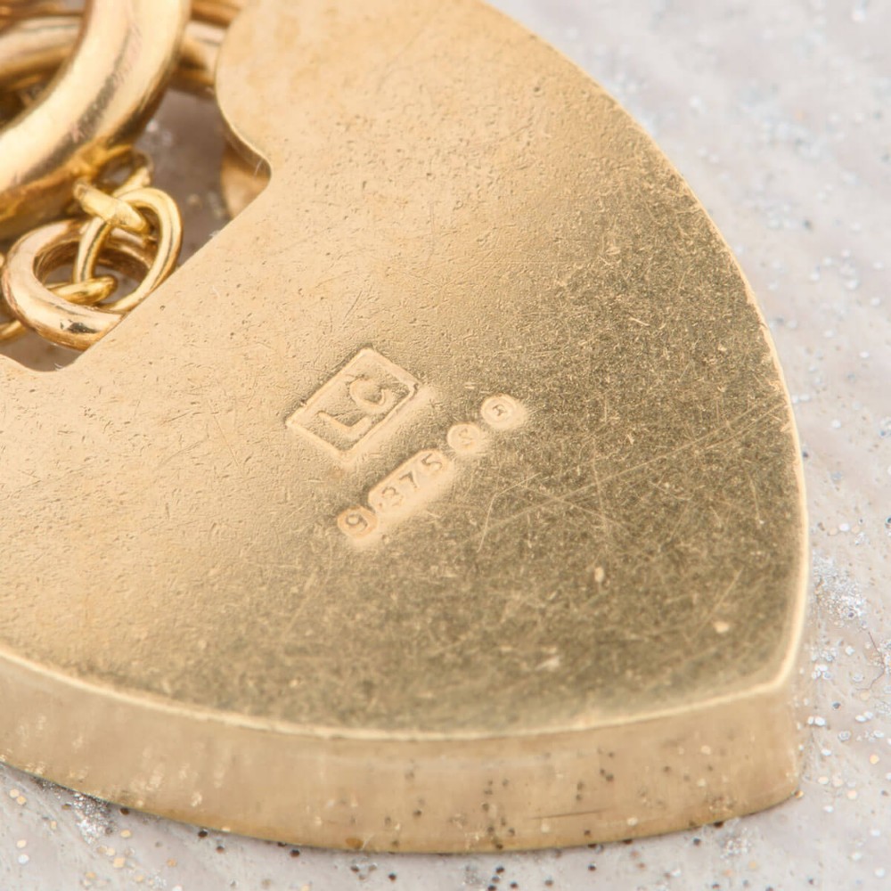 A 9ct rose gold curb chain bracelet featuring a heart-shaped padlock clasp with an attached safety chain. View VIII