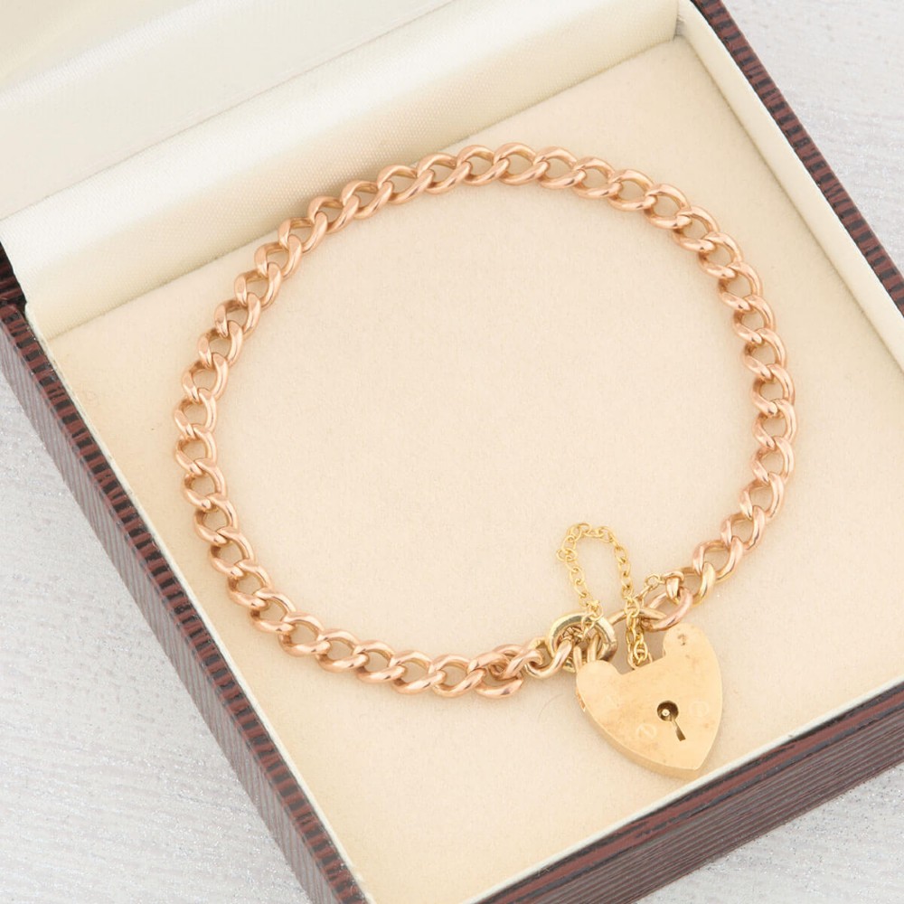 A 9ct rose gold curb chain bracelet featuring a heart-shaped padlock clasp with an attached safety chain. View IX