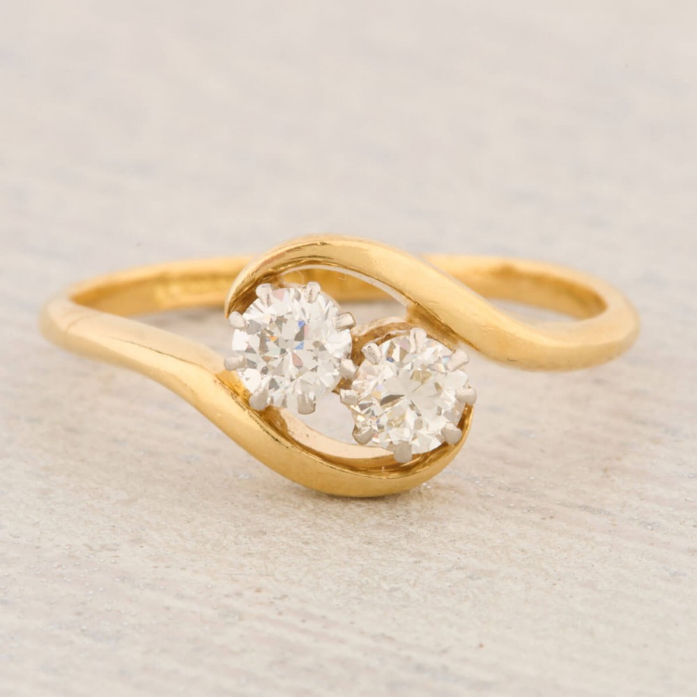 An 18ct yellow gold crossover bypass ring featuring two claw-set round brilliant diamonds.