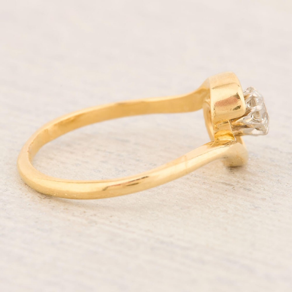 An 18ct yellow gold crossover bypass ring featuring two claw-set round brilliant diamonds. View IV