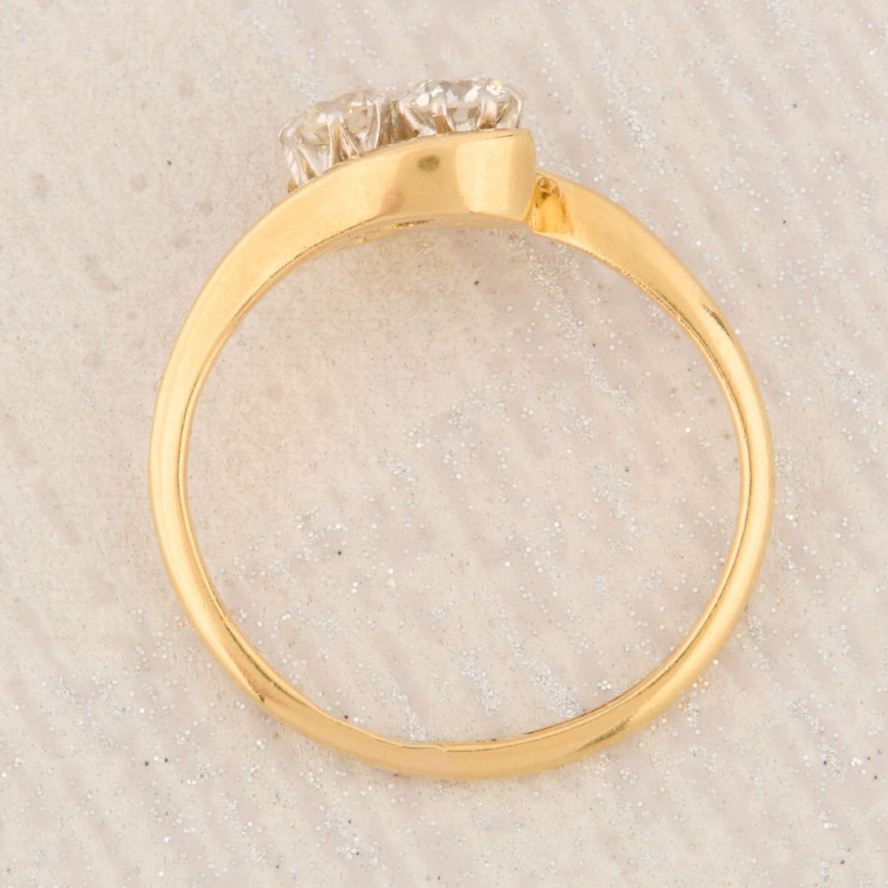 An 18ct yellow gold crossover bypass ring featuring two claw-set round brilliant diamonds. View VI