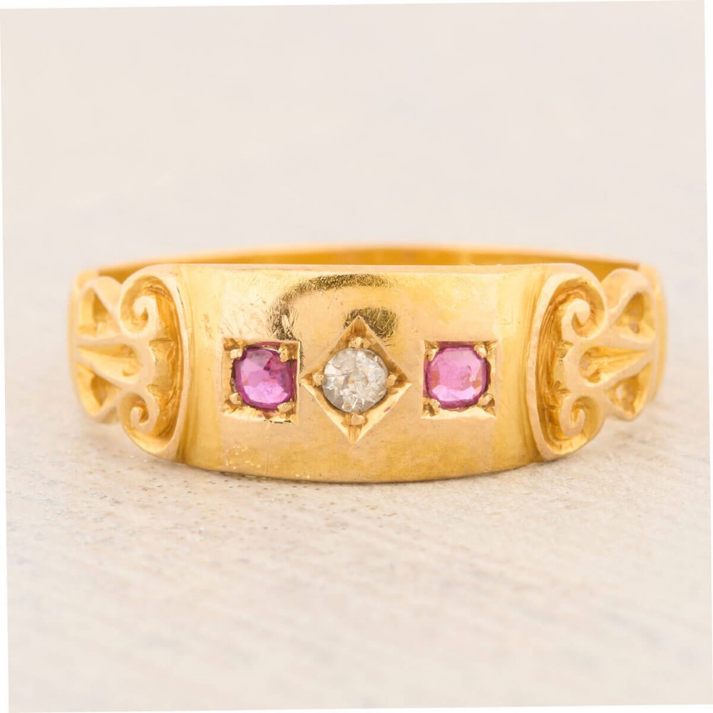 An 18ct yellow gold gypsy ring featuring a flush-set central diamond flanked by two rubies with carved scroll details.