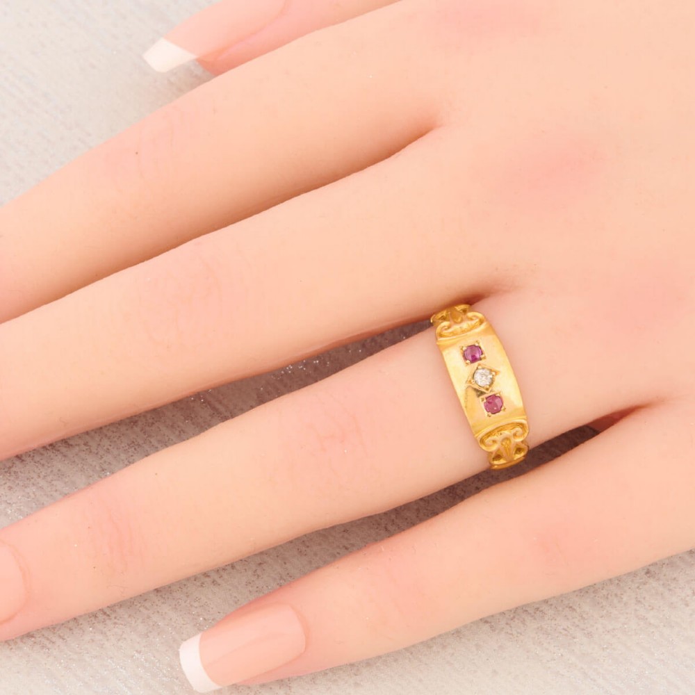An 18ct yellow gold gypsy ring featuring a flush-set central diamond flanked by two rubies with carved scroll details. View II