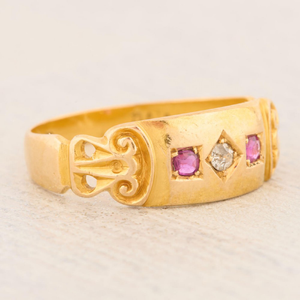 An 18ct yellow gold gypsy ring featuring a flush-set central diamond flanked by two rubies with carved scroll details. View III