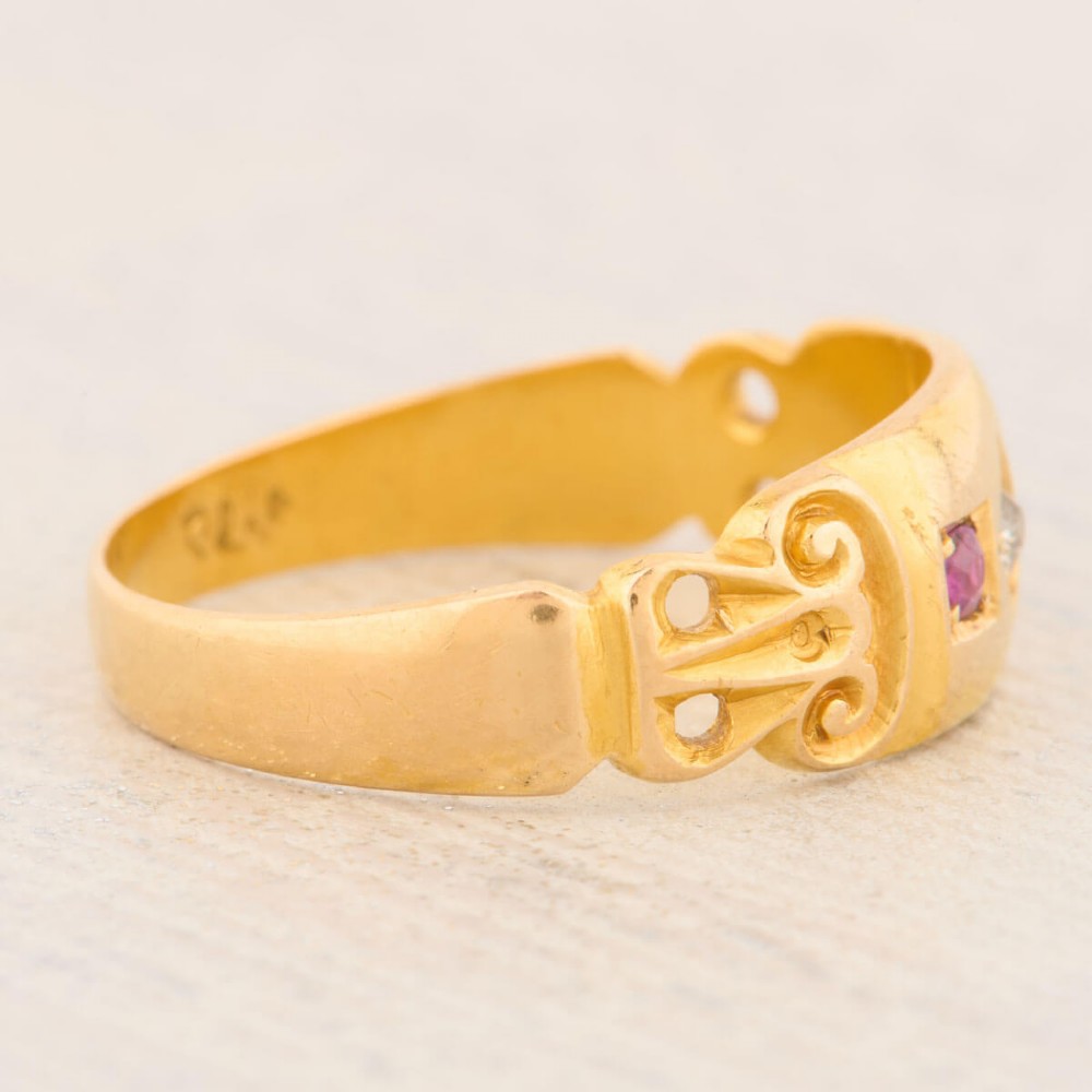 An 18ct yellow gold gypsy ring featuring a flush-set central diamond flanked by two rubies with carved scroll details. View IV