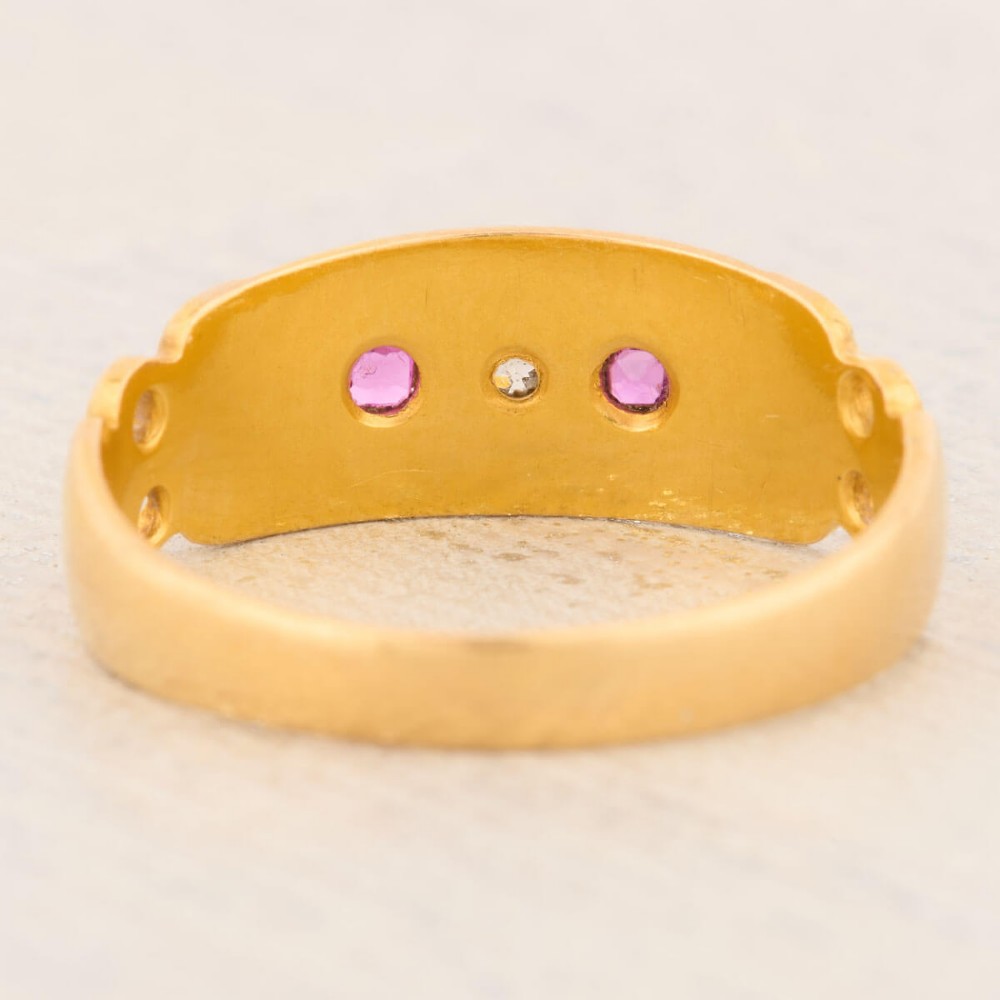 An 18ct yellow gold gypsy ring featuring a flush-set central diamond flanked by two rubies with carved scroll details. View V