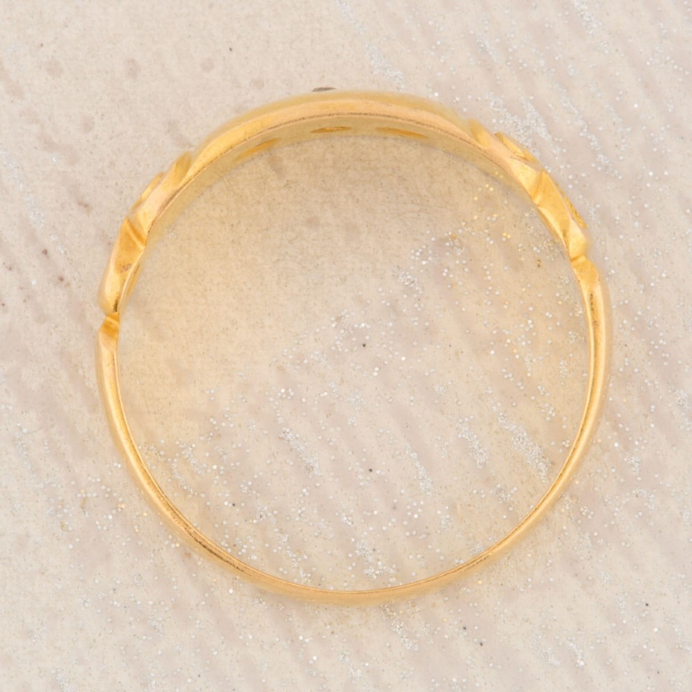 An 18ct yellow gold gypsy ring featuring a flush-set central diamond flanked by two rubies with carved scroll details. View VI