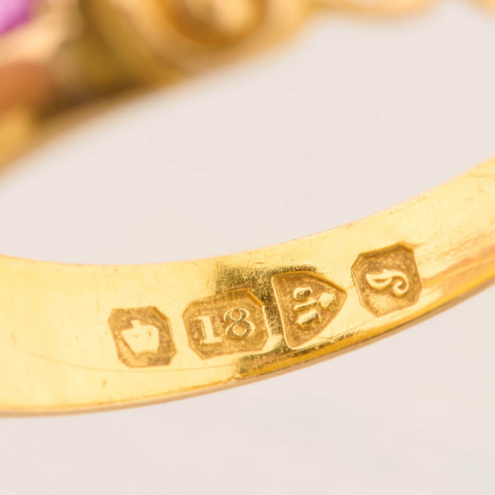 An 18ct yellow gold gypsy ring featuring a flush-set central diamond flanked by two rubies with carved scroll details. View VII