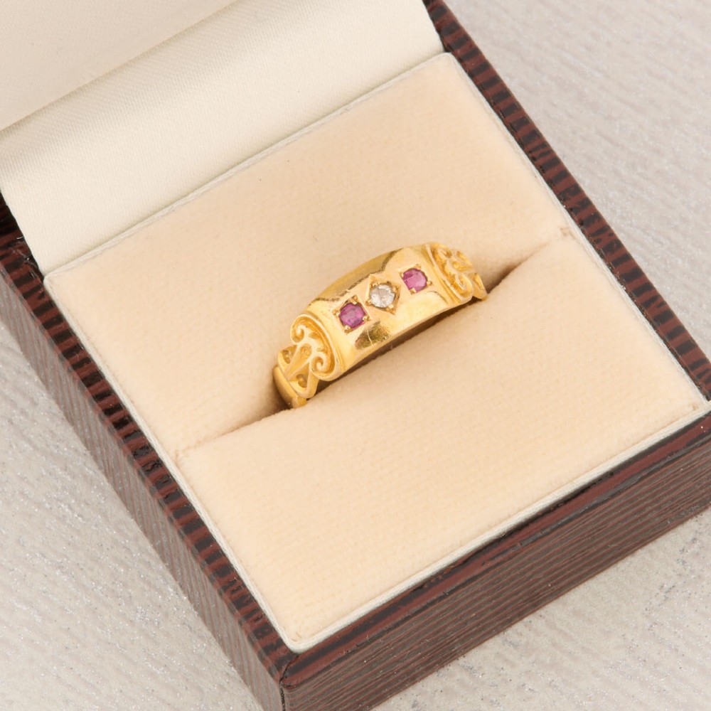 An 18ct yellow gold gypsy ring featuring a flush-set central diamond flanked by two rubies with carved scroll details. View VIII