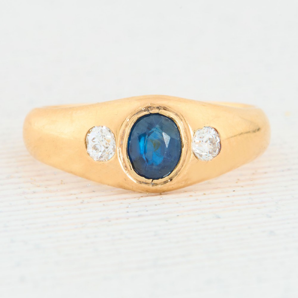 An 18ct yellow gold band features a central oval blue sapphire flanked by two flush-set round diamonds.