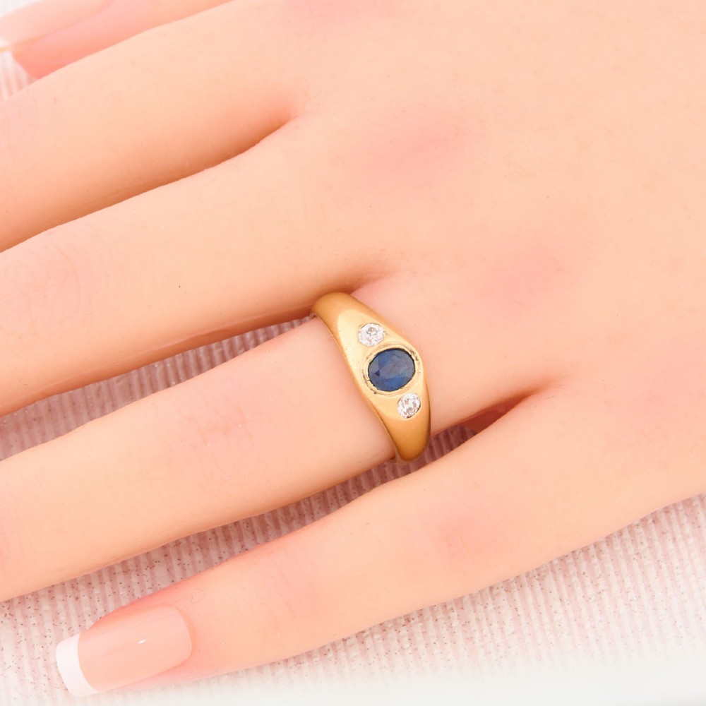 An 18ct yellow gold band features a central oval blue sapphire flanked by two flush-set round diamonds. View II
