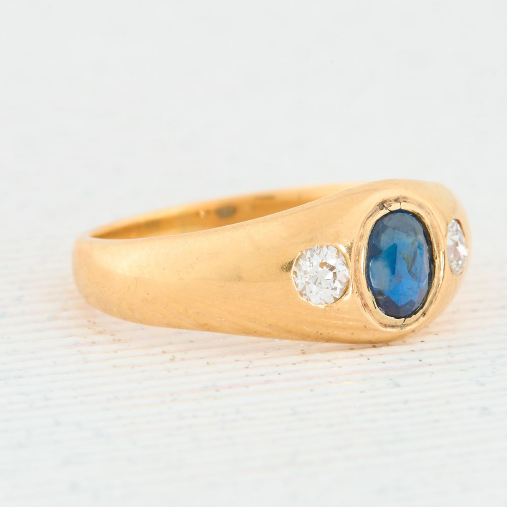An 18ct yellow gold band features a central oval blue sapphire flanked by two flush-set round diamonds. View III