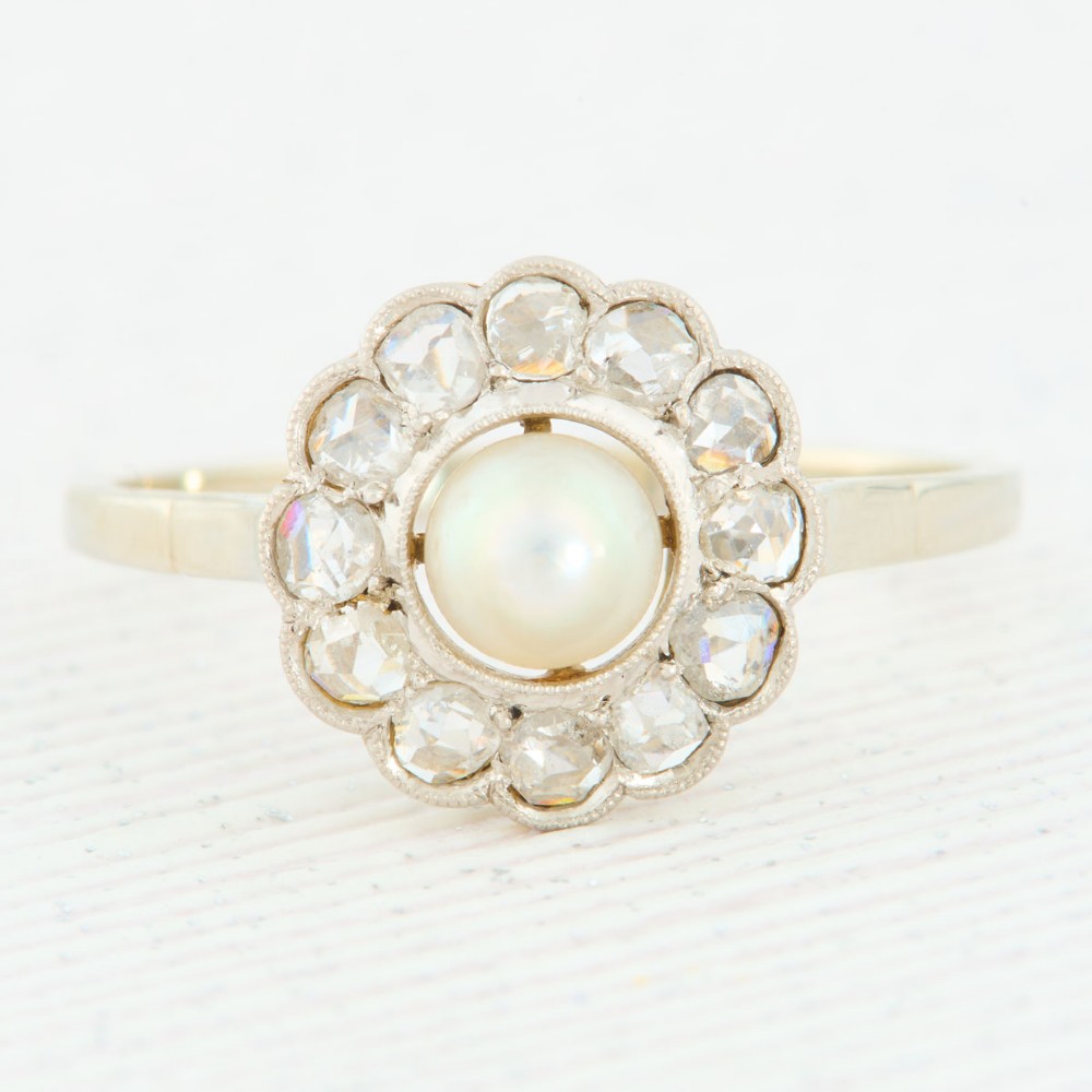 An 18ct white gold cluster ring featuring a central round pearl encircled by a halo of small diamonds with millegrain edging.