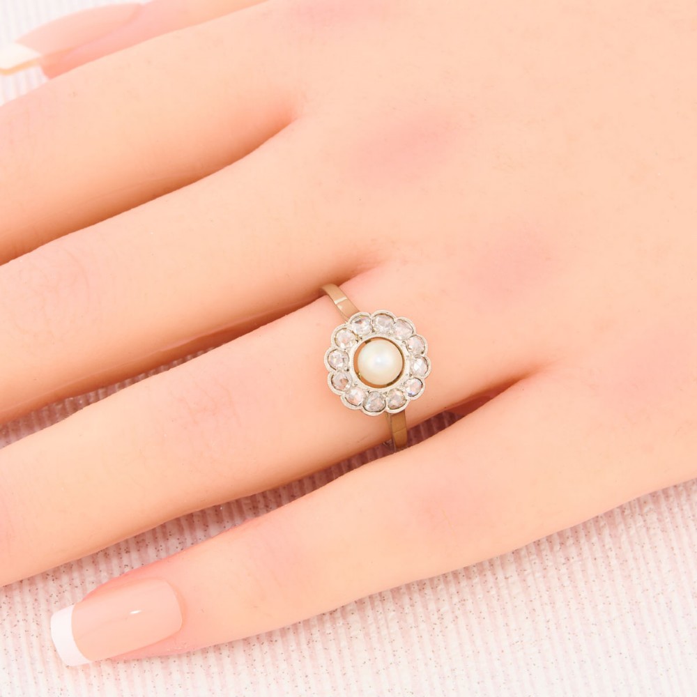 An 18ct white gold cluster ring featuring a central round pearl encircled by a halo of small diamonds with millegrain edging. View II