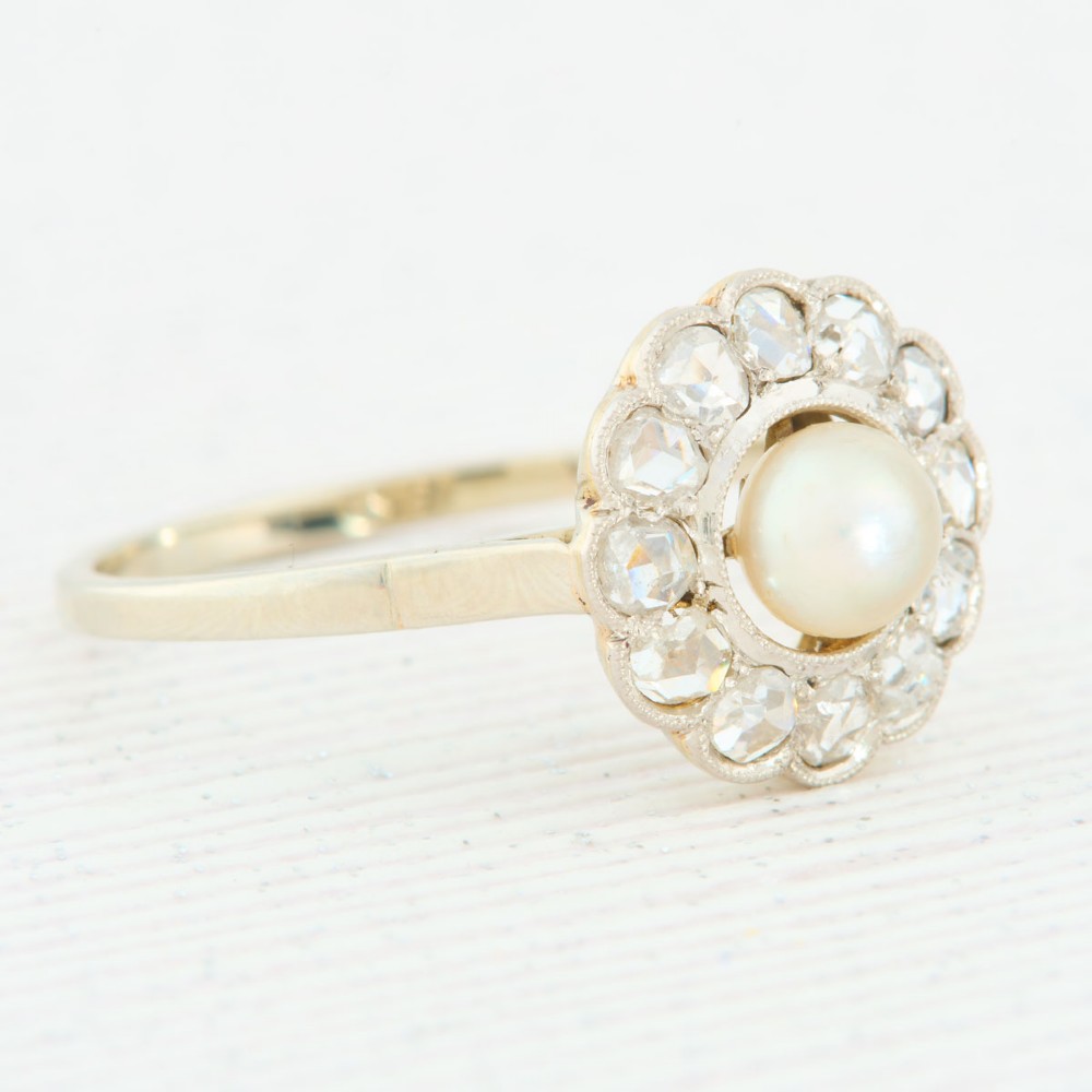 An 18ct white gold cluster ring featuring a central round pearl encircled by a halo of small diamonds with millegrain edging. View III