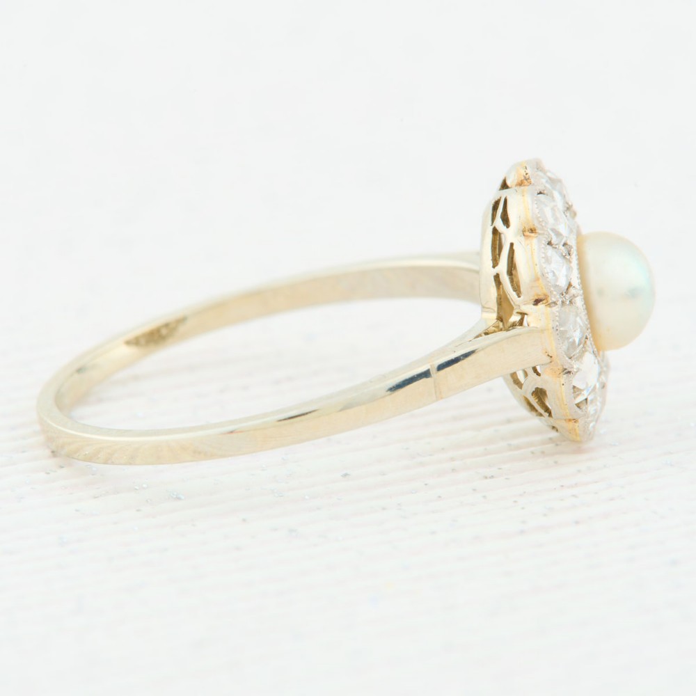An 18ct white gold cluster ring featuring a central round pearl encircled by a halo of small diamonds with millegrain edging. View IV
