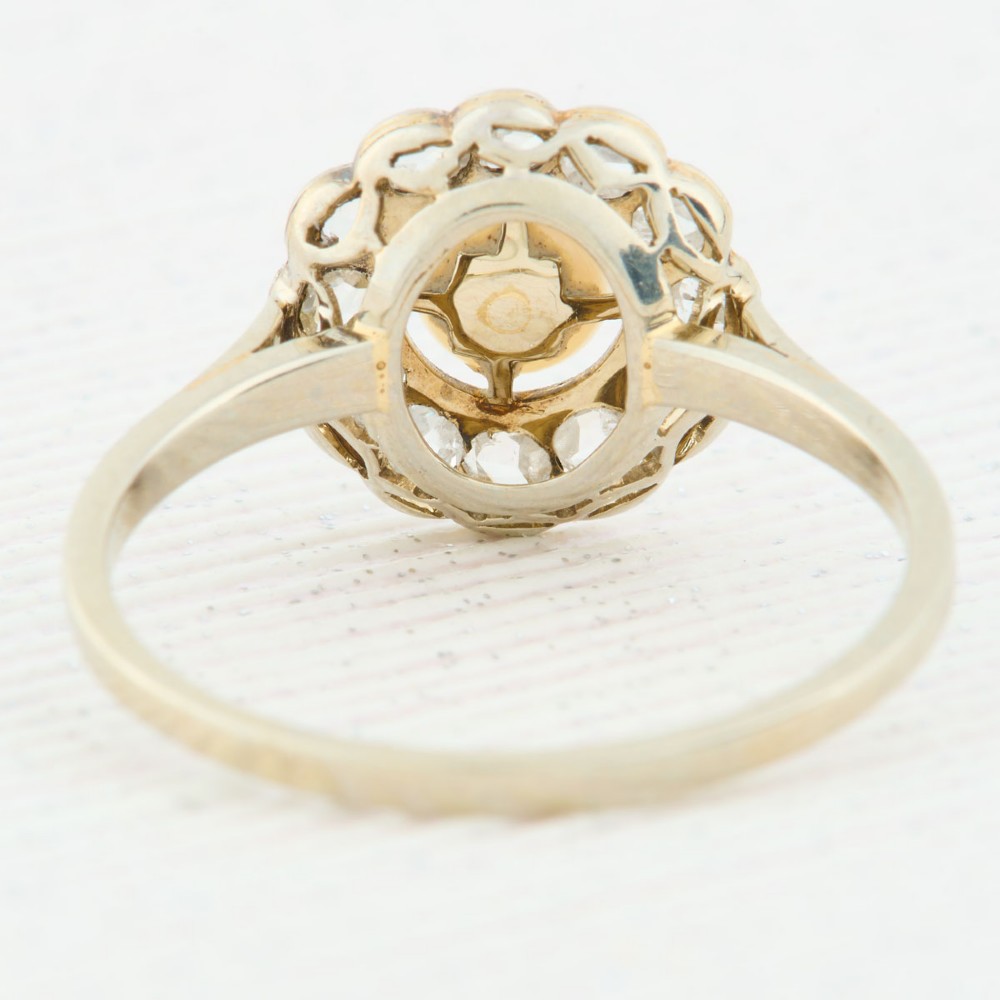 An 18ct white gold cluster ring featuring a central round pearl encircled by a halo of small diamonds with millegrain edging. View V