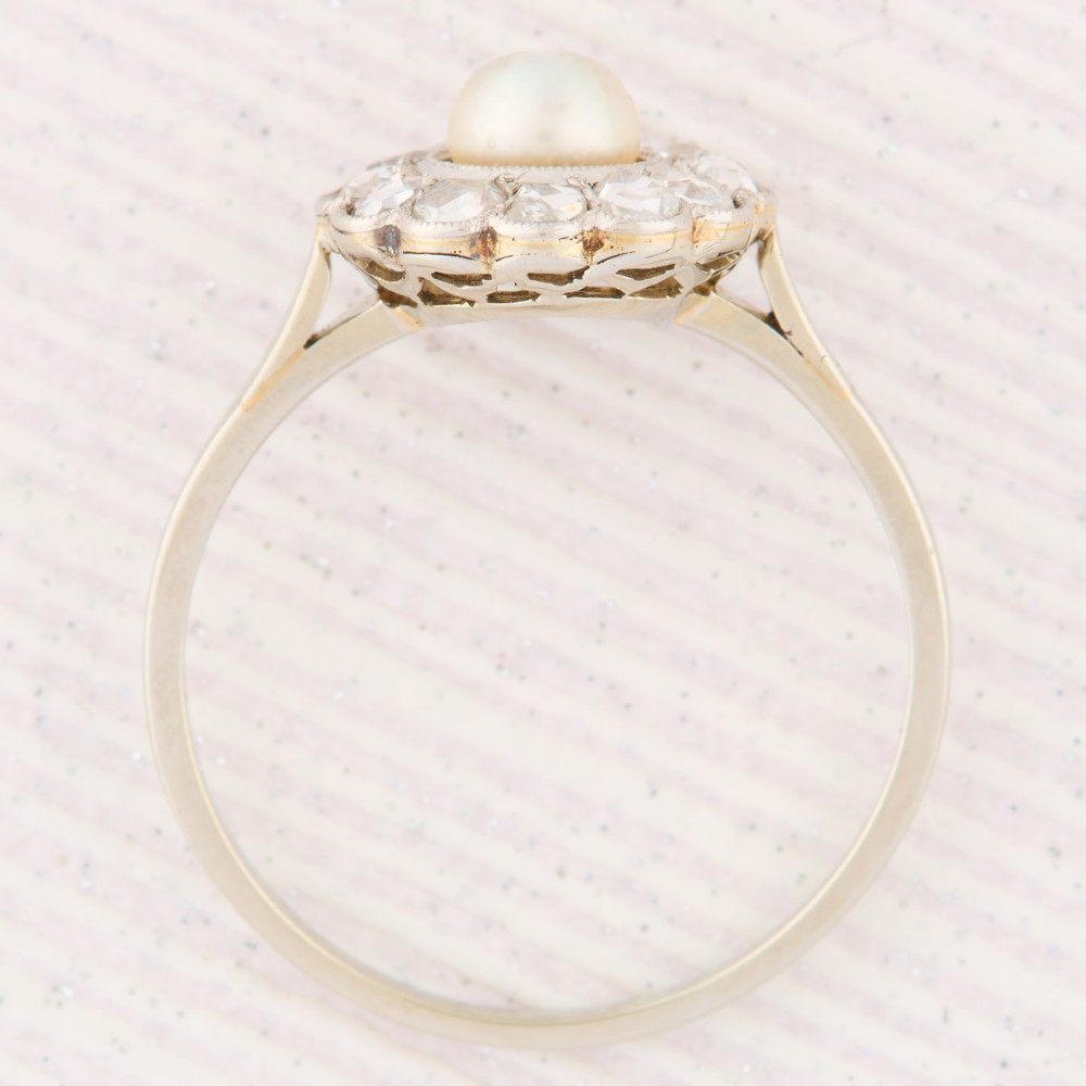 An 18ct white gold cluster ring featuring a central round pearl encircled by a halo of small diamonds with millegrain edging. View VI