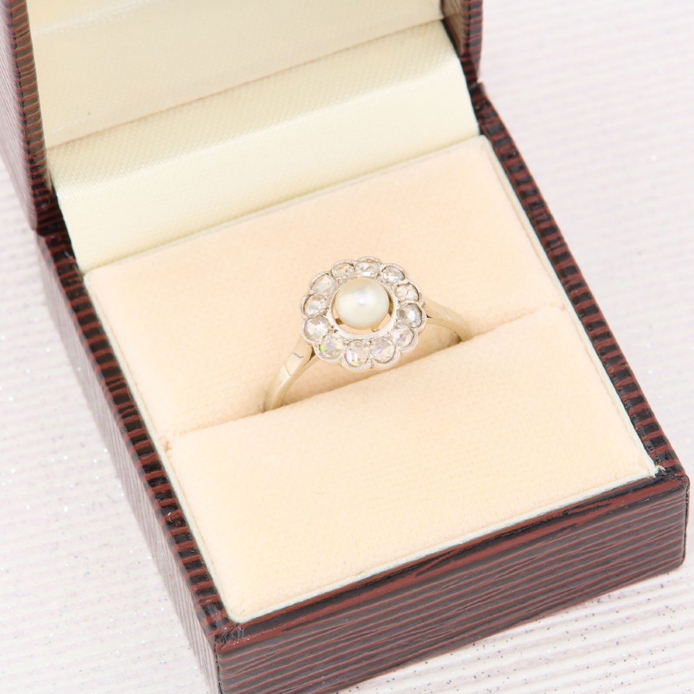An 18ct white gold cluster ring featuring a central round pearl encircled by a halo of small diamonds with millegrain edging. View VII