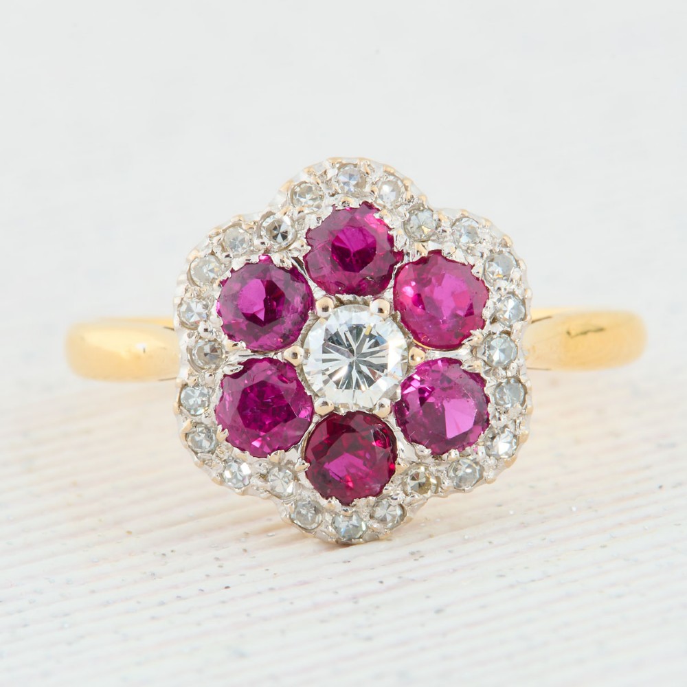 An 18ct yellow gold cluster ring with a brilliant central diamond surrounded by six round rubies and an outer diamond halo.