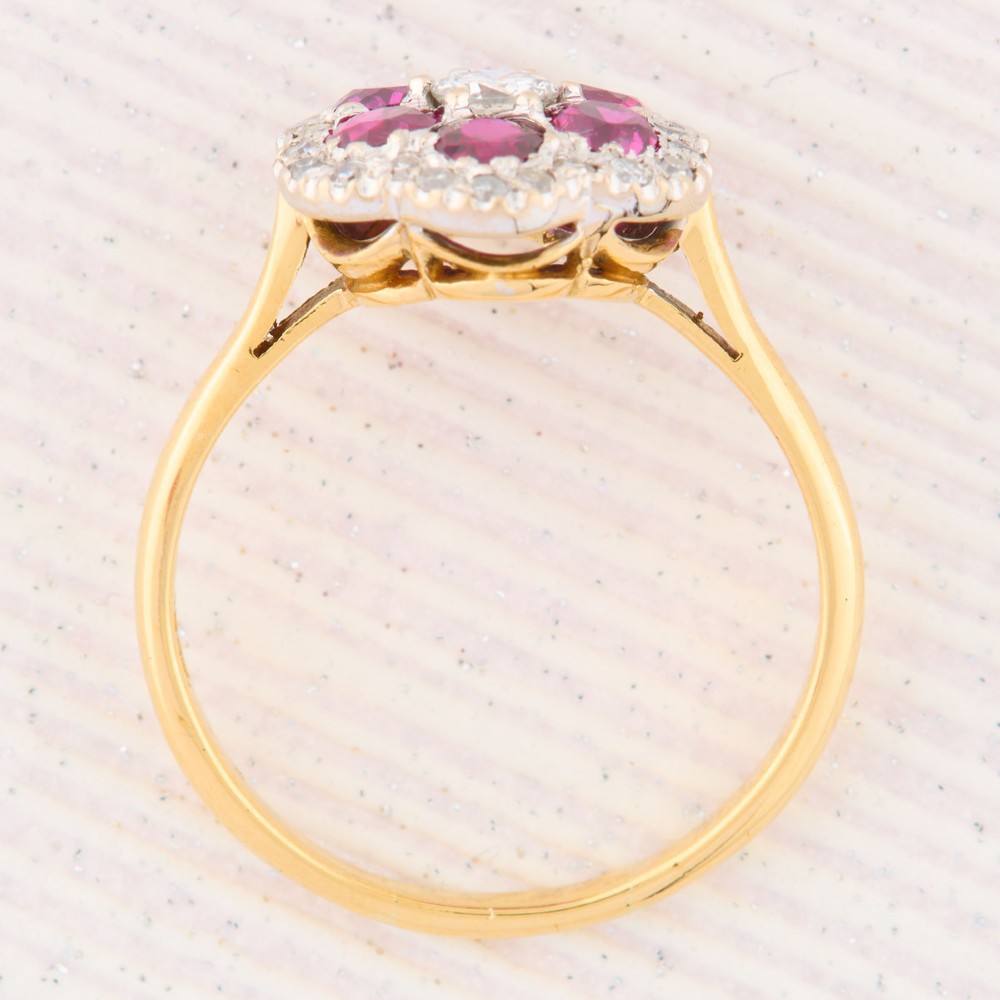 An 18ct yellow gold cluster ring with a brilliant central diamond surrounded by six round rubies and an outer diamond halo. View VI
