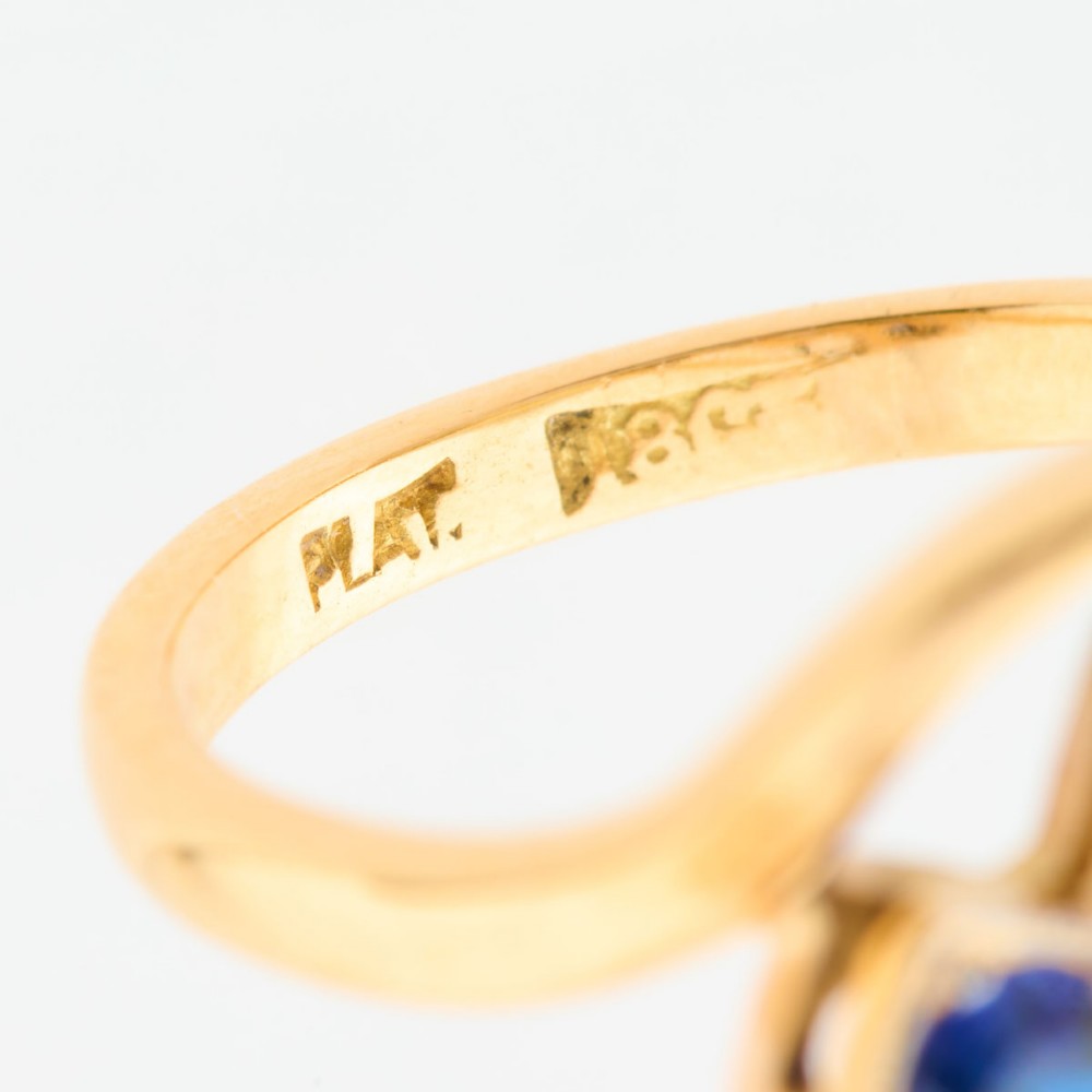 An Art Deco 18ct yellow gold dress ring featuring a central round diamond flanked by two round blue sapphires set diagonally in square millegrain mounts within a bypass band. View VII