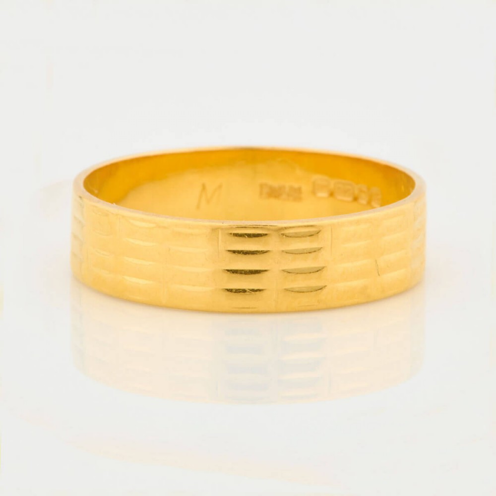 A wide 22ct yellow gold wedding ring featuring an engraved ribbed geometric pattern along the exterior surface and internal hallmarks.