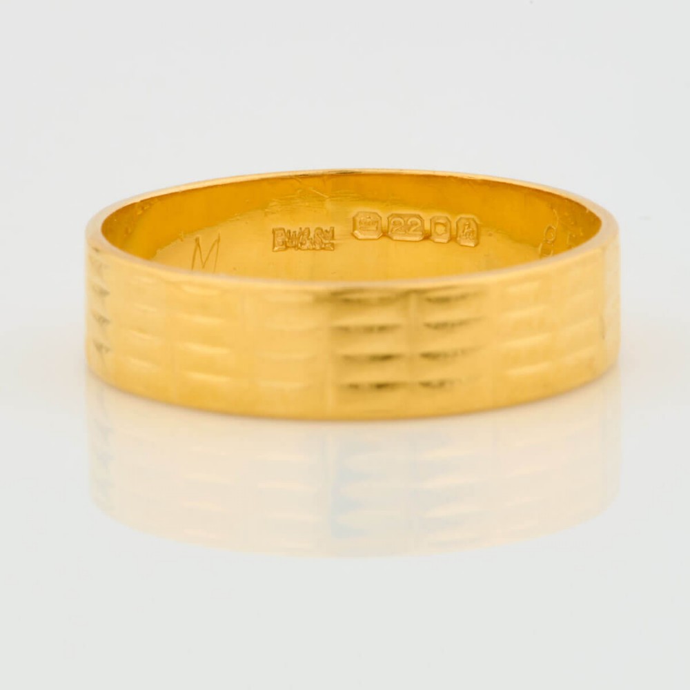 A wide 22ct yellow gold wedding ring featuring an engraved ribbed geometric pattern along the exterior surface and internal hallmarks. View III