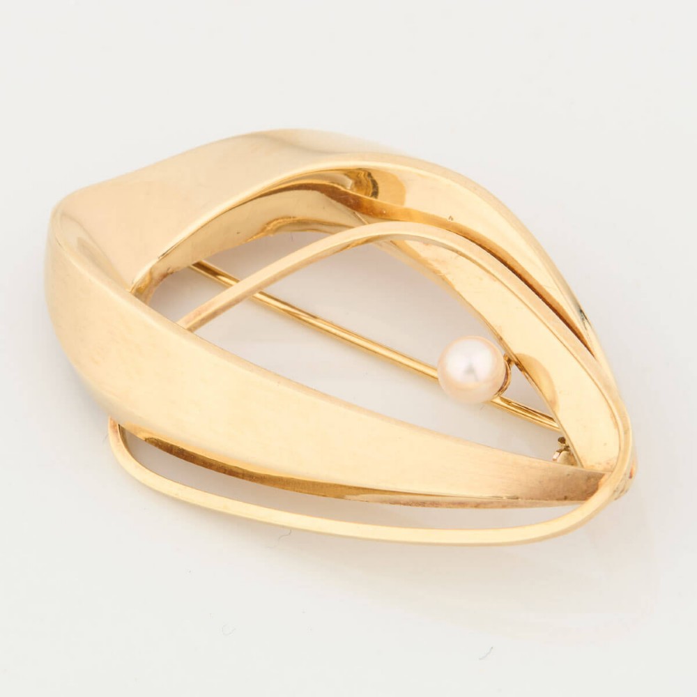 A 9ct gold brooch featuring a sweeping, abstract curved frame holding a single white pearl at its centre.
