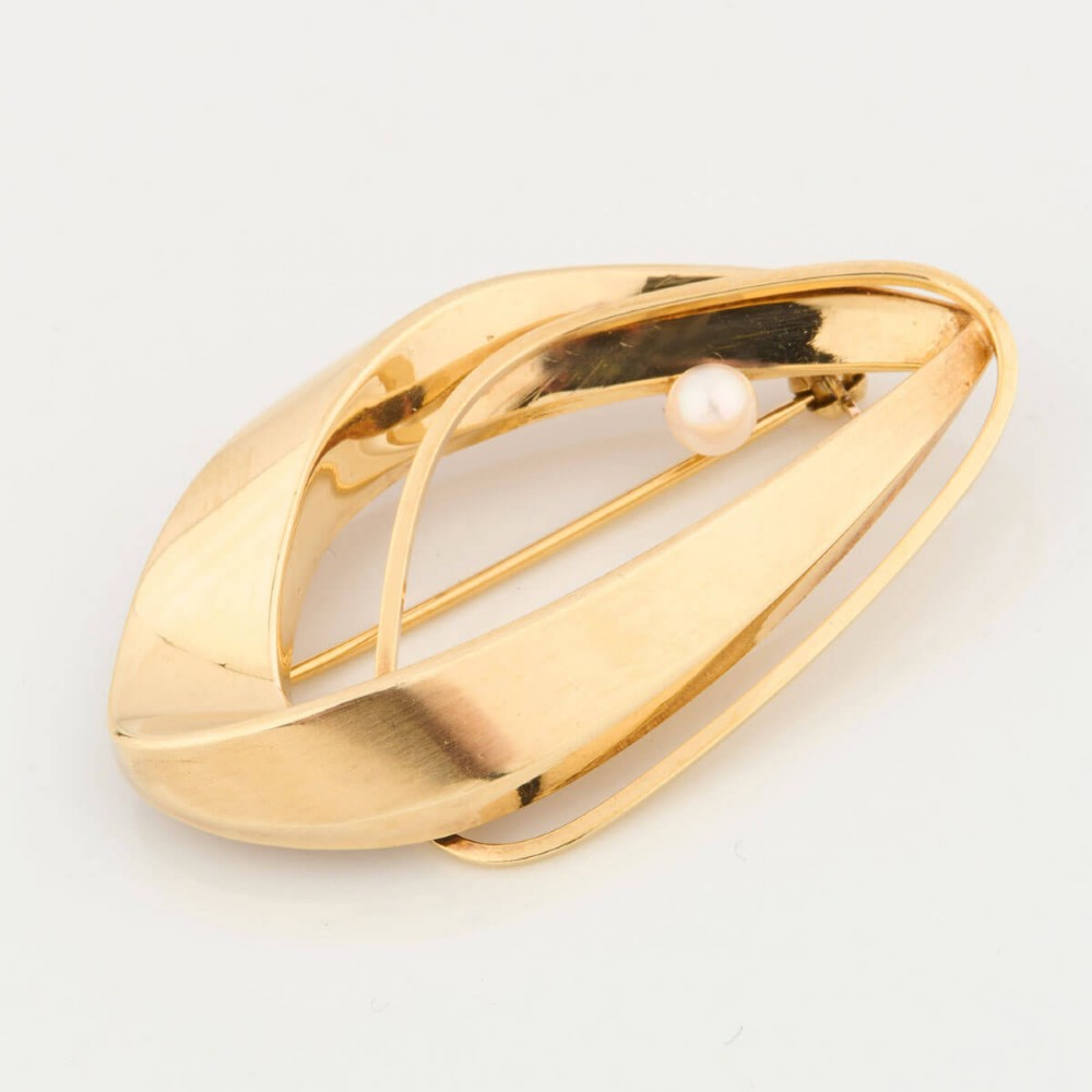 A 9ct gold brooch featuring a sweeping, abstract curved frame holding a single white pearl at its centre. View II
