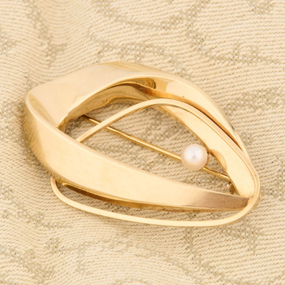 A 9ct gold brooch featuring a sweeping, abstract curved frame holding a single white pearl at its centre. View VI