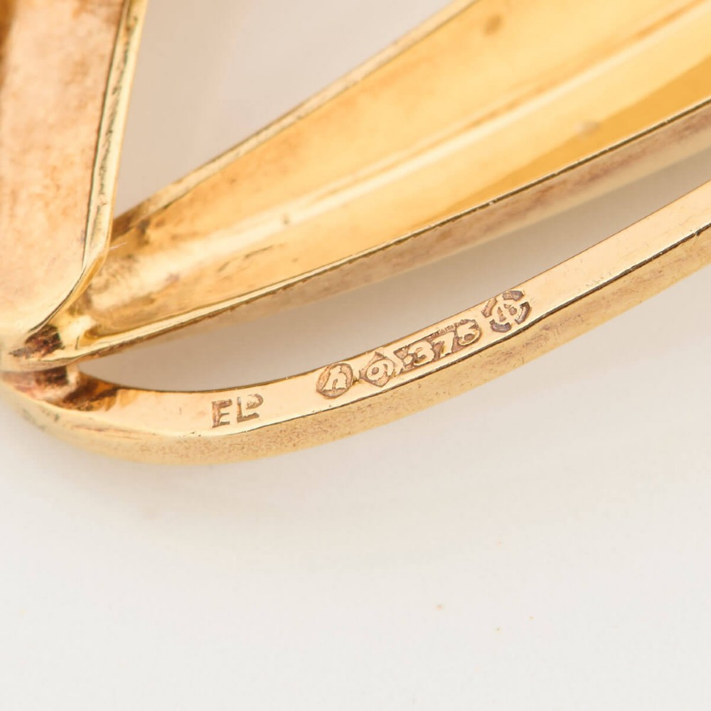 A 9ct gold brooch featuring a sweeping, abstract curved frame holding a single white pearl at its centre. View VII