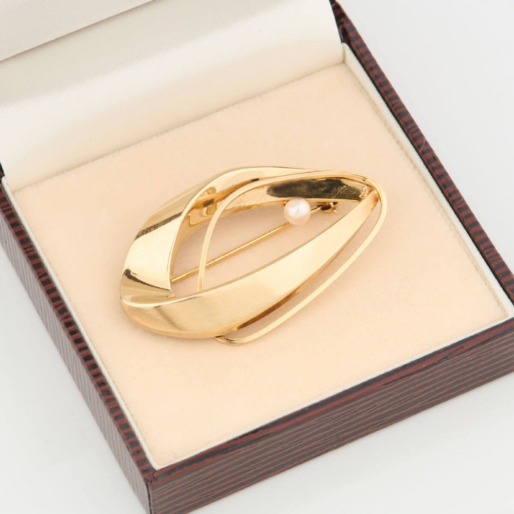A 9ct gold brooch featuring a sweeping, abstract curved frame holding a single white pearl at its centre. View VIII