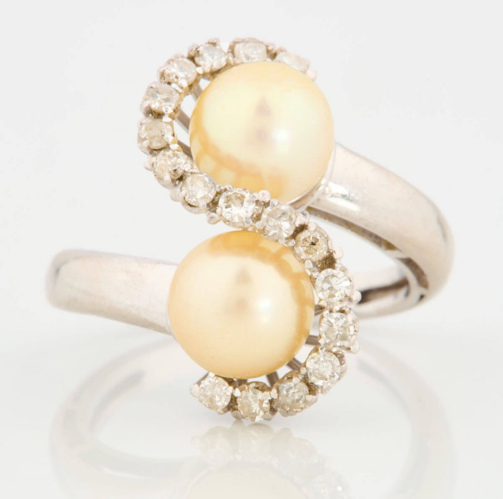 An 18ct white gold swirl cocktail ring featuring two central cream pearls wrapped in an S-shaped band set with small round diamonds.