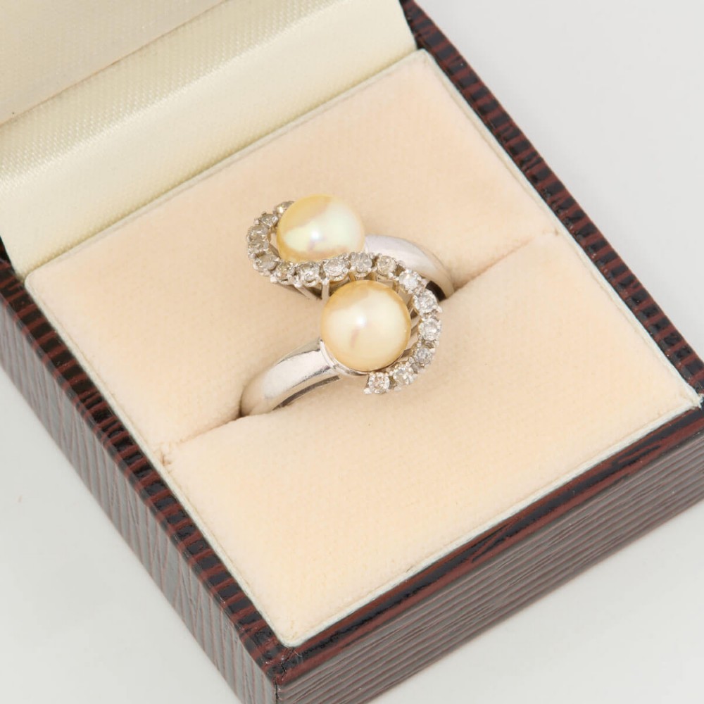 An 18ct white gold swirl cocktail ring featuring two central cream pearls wrapped in an S-shaped band set with small round diamonds. View VII