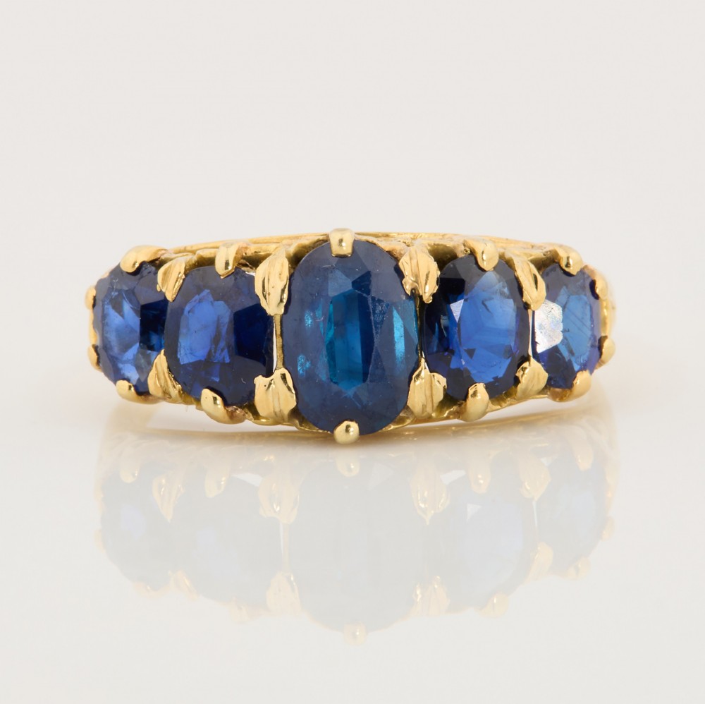An eighteen-carat yellow gold ring featuring five graduated oval blue sapphires set in a carved claw setting.