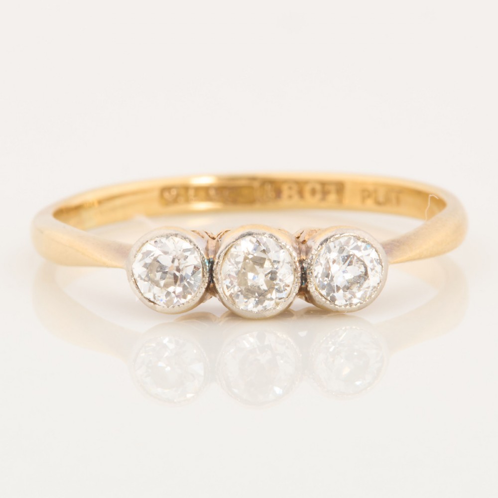 An 18ct yellow gold trilogy ring featuring three round diamonds set in platinum rub-over settings.