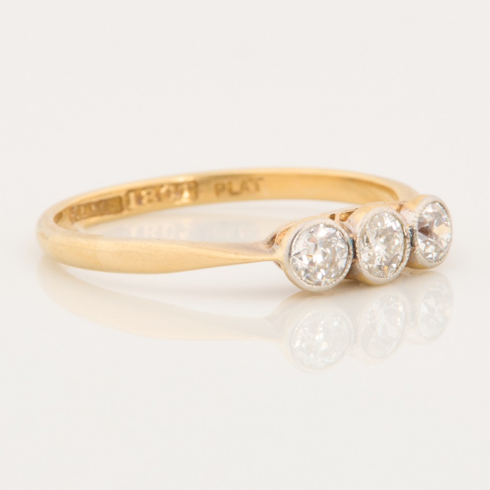 An 18ct yellow gold trilogy ring featuring three round diamonds set in platinum rub-over settings. View III