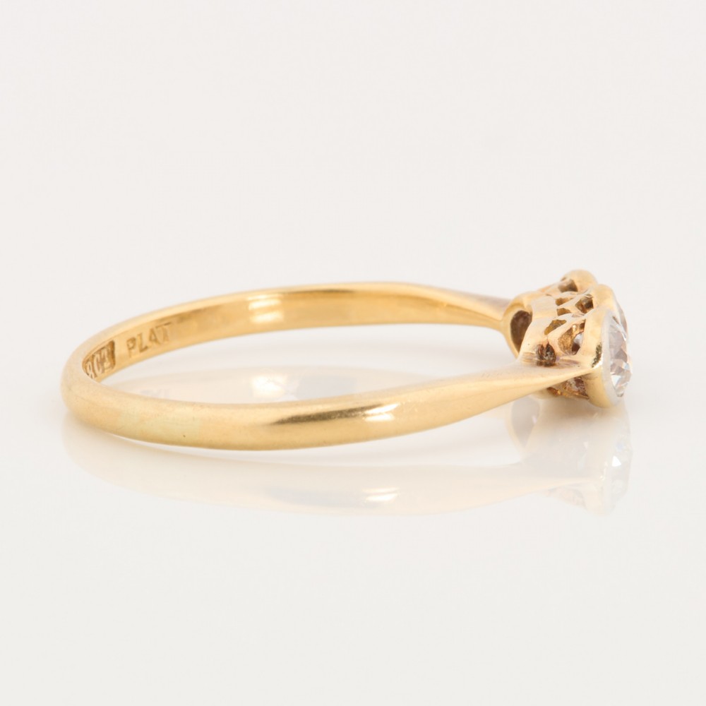 An 18ct yellow gold trilogy ring featuring three round diamonds set in platinum rub-over settings. View IV