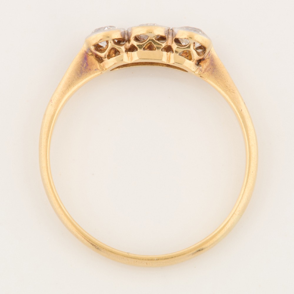 An 18ct yellow gold trilogy ring featuring three round diamonds set in platinum rub-over settings. View VI