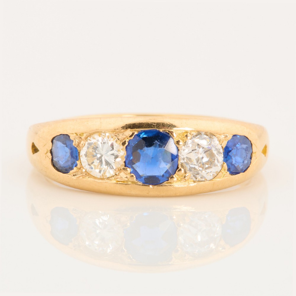 An 18ct yellow gold five-stone ring featuring three round blue sapphires alternating with two round diamonds in a carved boat-style gallery.