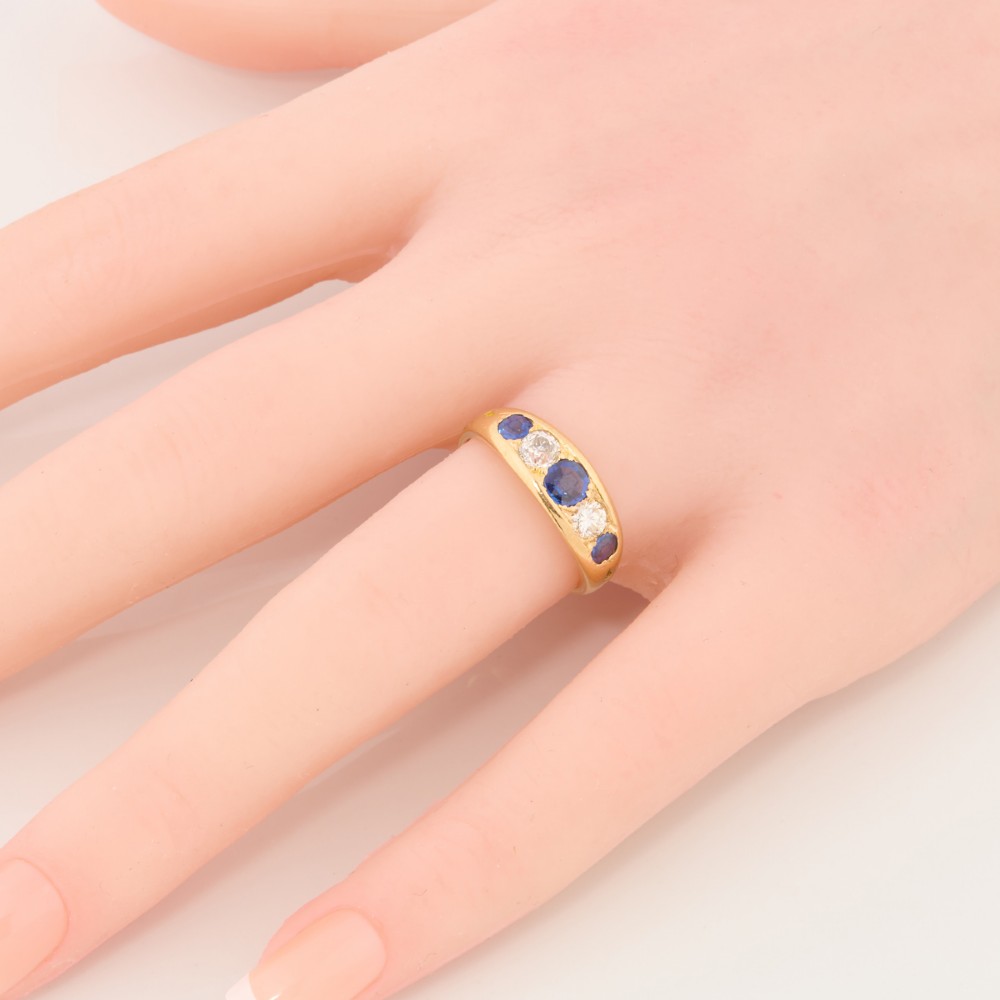 An 18ct yellow gold five-stone ring featuring three round blue sapphires alternating with two round diamonds in a carved boat-style gallery. View II