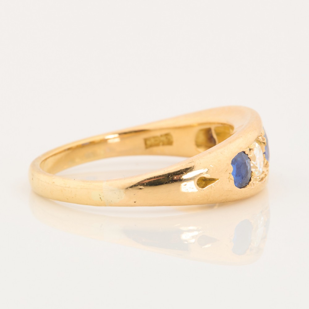 An 18ct yellow gold five-stone ring featuring three round blue sapphires alternating with two round diamonds in a carved boat-style gallery. View IV