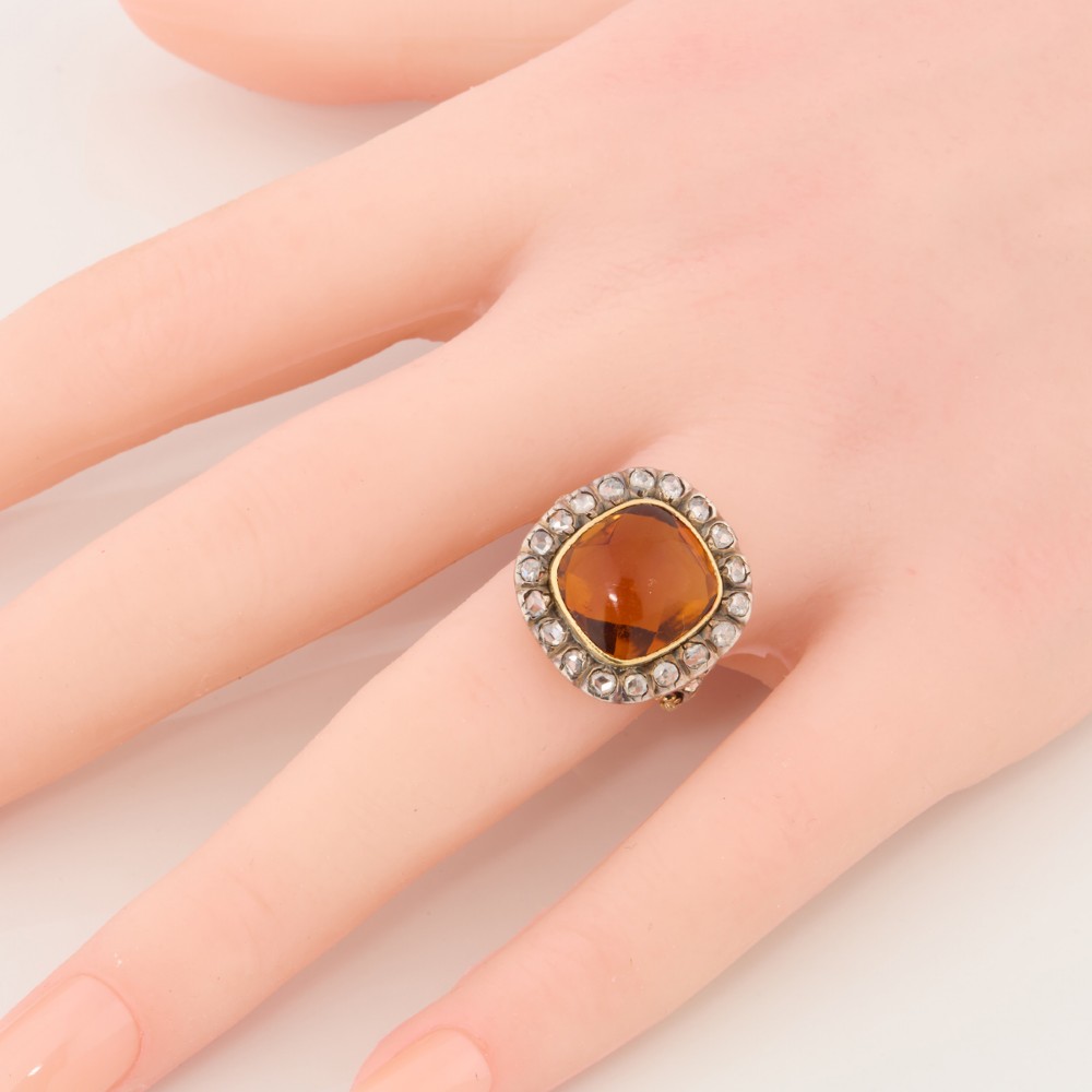 An antique 18ct gold ring set with a central cushion-cut amber citrine encircled by a halo of diamonds with decorative scrollwork shoulders. View II