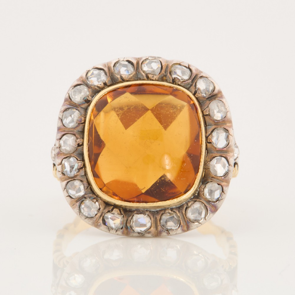 An antique 18ct gold ring set with a central cushion-cut amber citrine encircled by a halo of diamonds with decorative scrollwork shoulders. View III