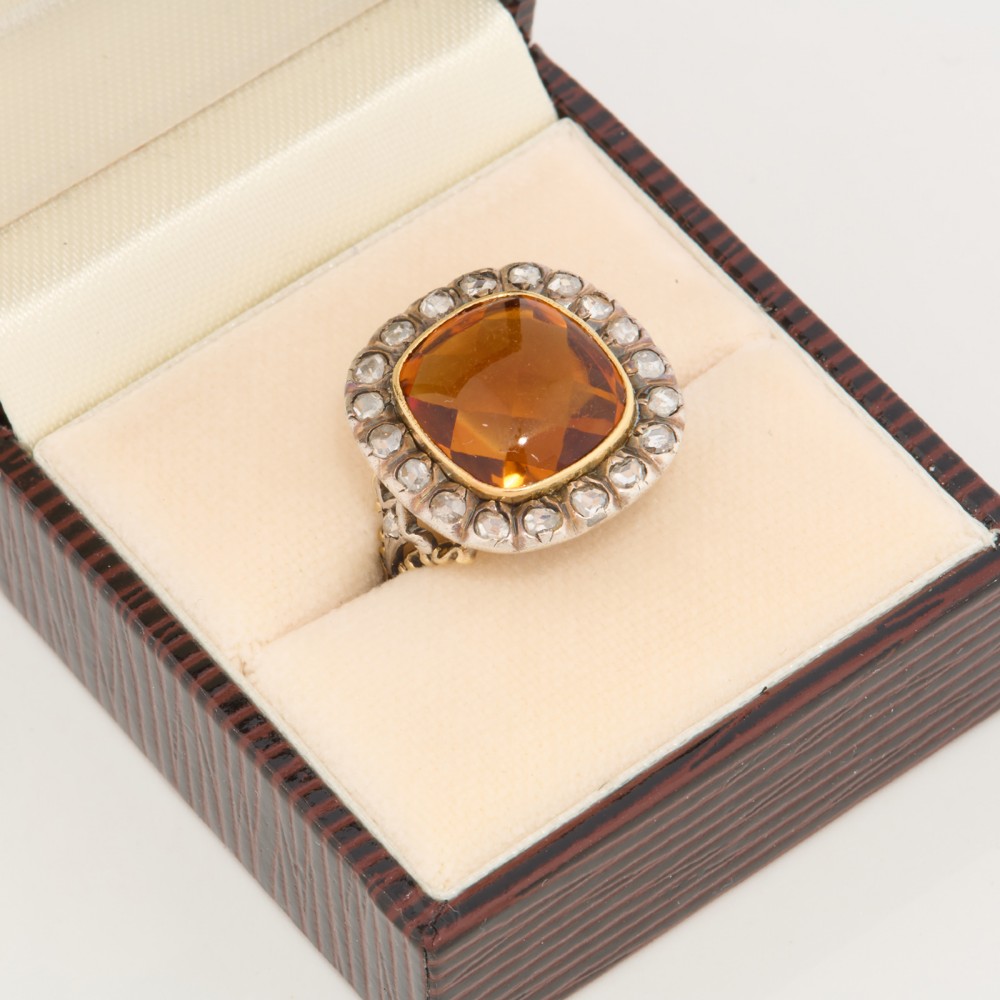 An antique 18ct gold ring set with a central cushion-cut amber citrine encircled by a halo of diamonds with decorative scrollwork shoulders. View VII