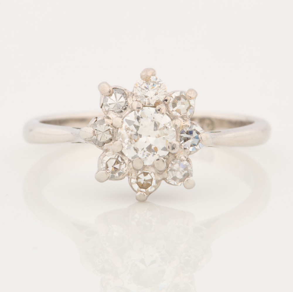 An 18ct white gold ring featuring a central round diamond encircled by eight smaller diamonds in a daisy cluster design.