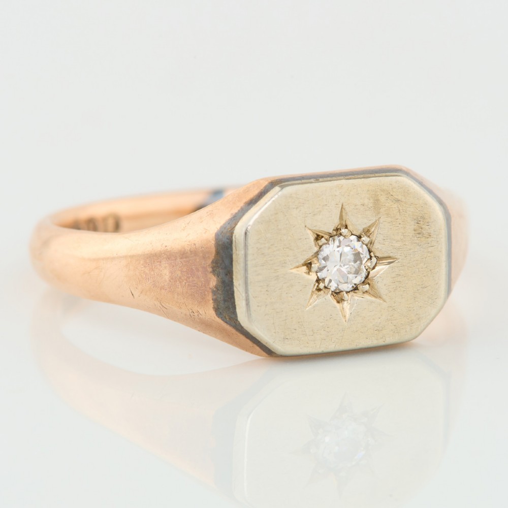 A 9ct yellow gold signet ring featuring an octagonal face with a starburst-set diamond in the centre.
