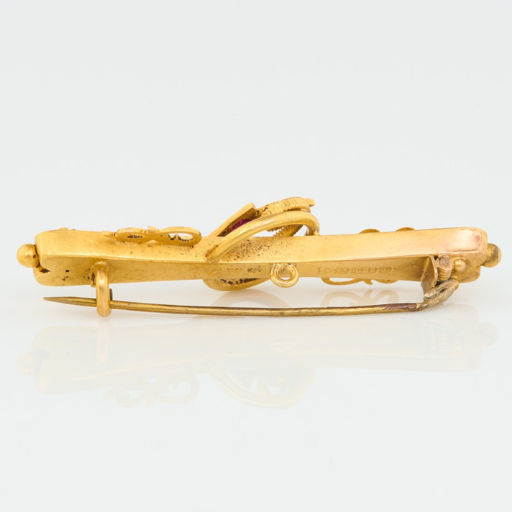 A yellow gold bar brooch featuring carved leaf detail, a central circular wire ring, and a central ruby flanked by two diamonds. View IV