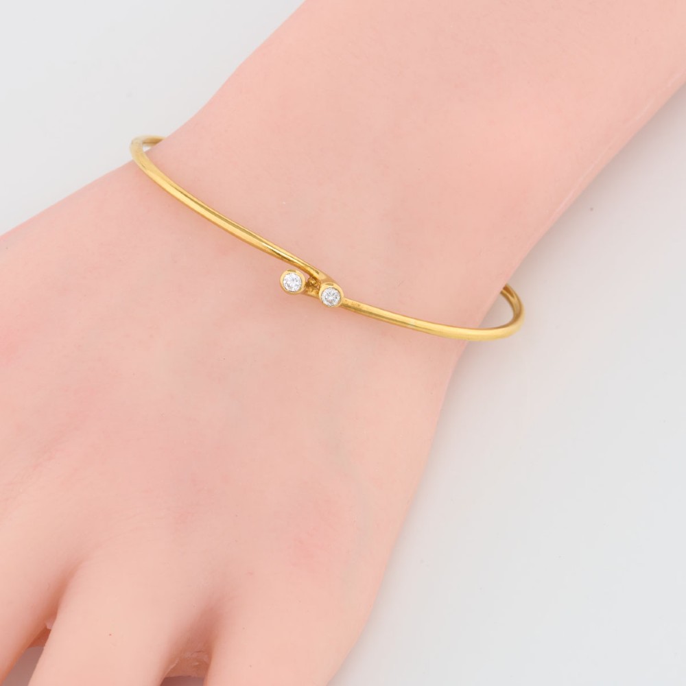 A slim 18ct yellow gold crossover bangle featuring two bezel-set diamonds at the open ends and an attached safety chain. View II